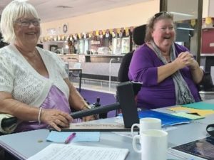 Two women sitting next to each other at a table laughing.