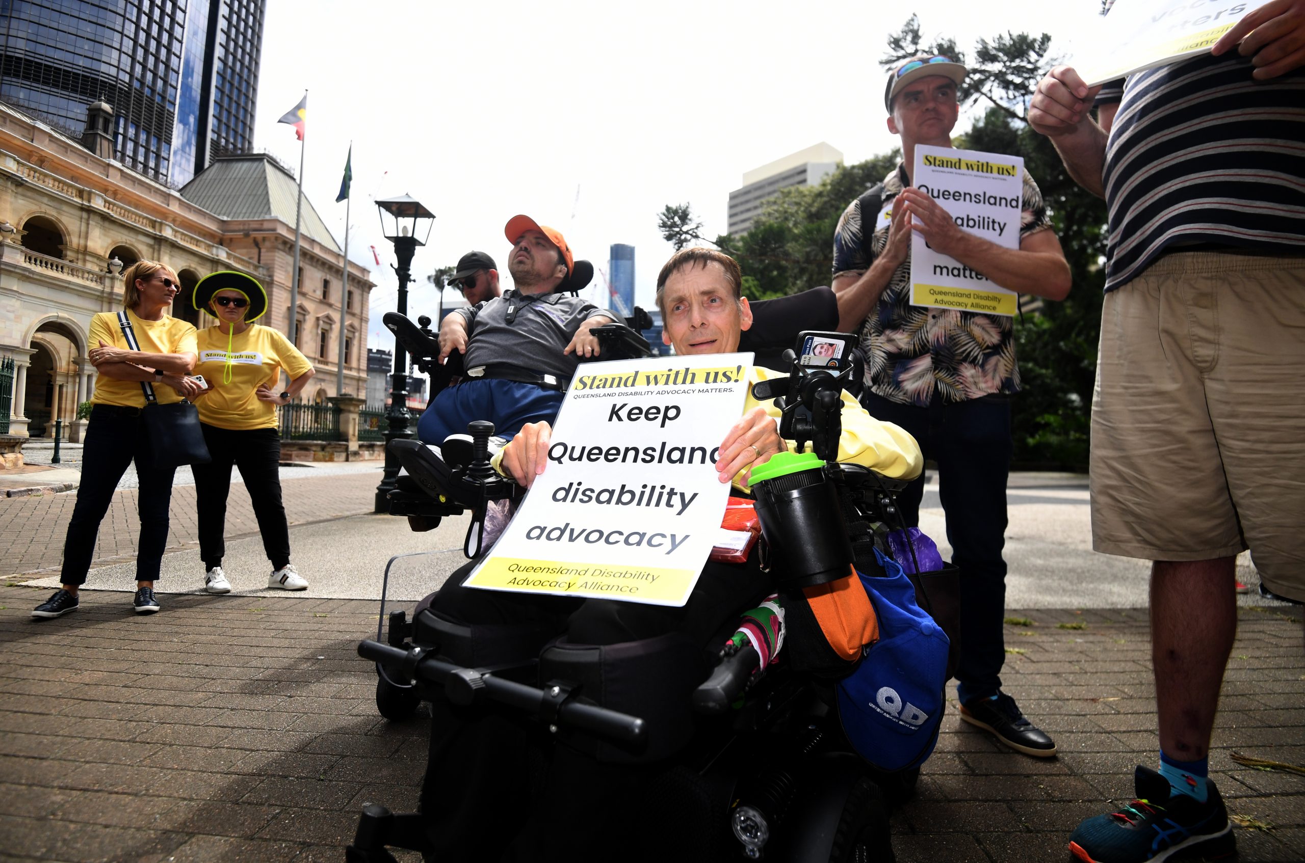 A man in a wheelchair holding a sign which says Keep Queensland disability advocacy.