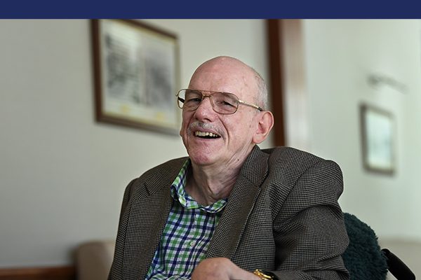A man wearing a jacket and buttoned up shirt and wearing glasses and smiling at the camera.