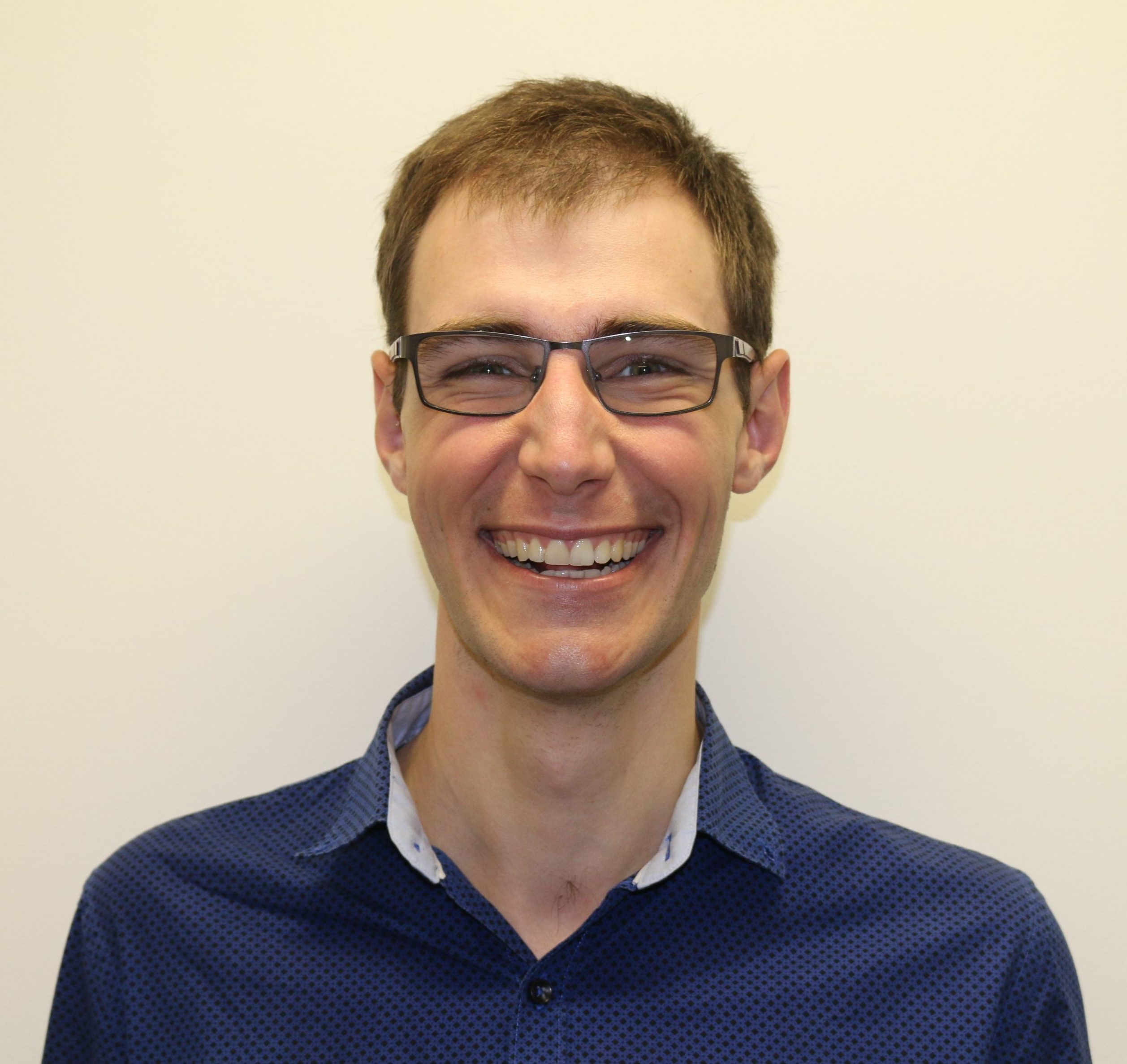 A man in a dark blue business shirt and glasses, smiling at the camera.