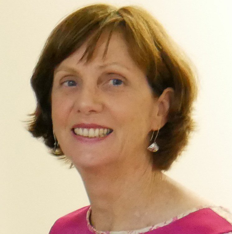 A woman with short brown hair, wearing a pink shirt and smiling at the camera.