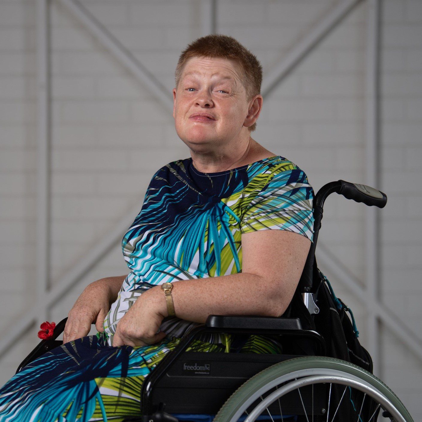 A woman with short red hair, wearing a blue and green floral dress looking at the camera.