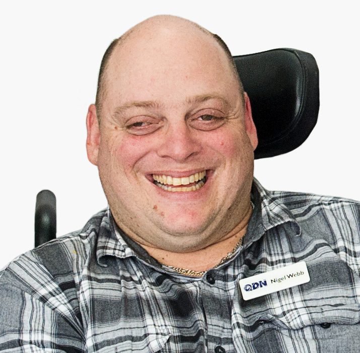 A man with a checked button up grey and white shirt, smiling at the camera.