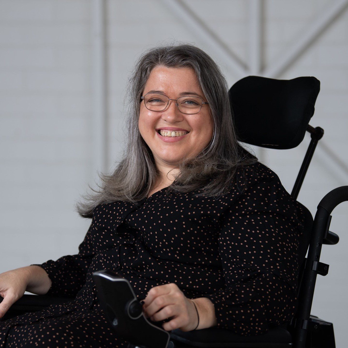 A lady wearing all black with long hair and glasses smiling at the camera.