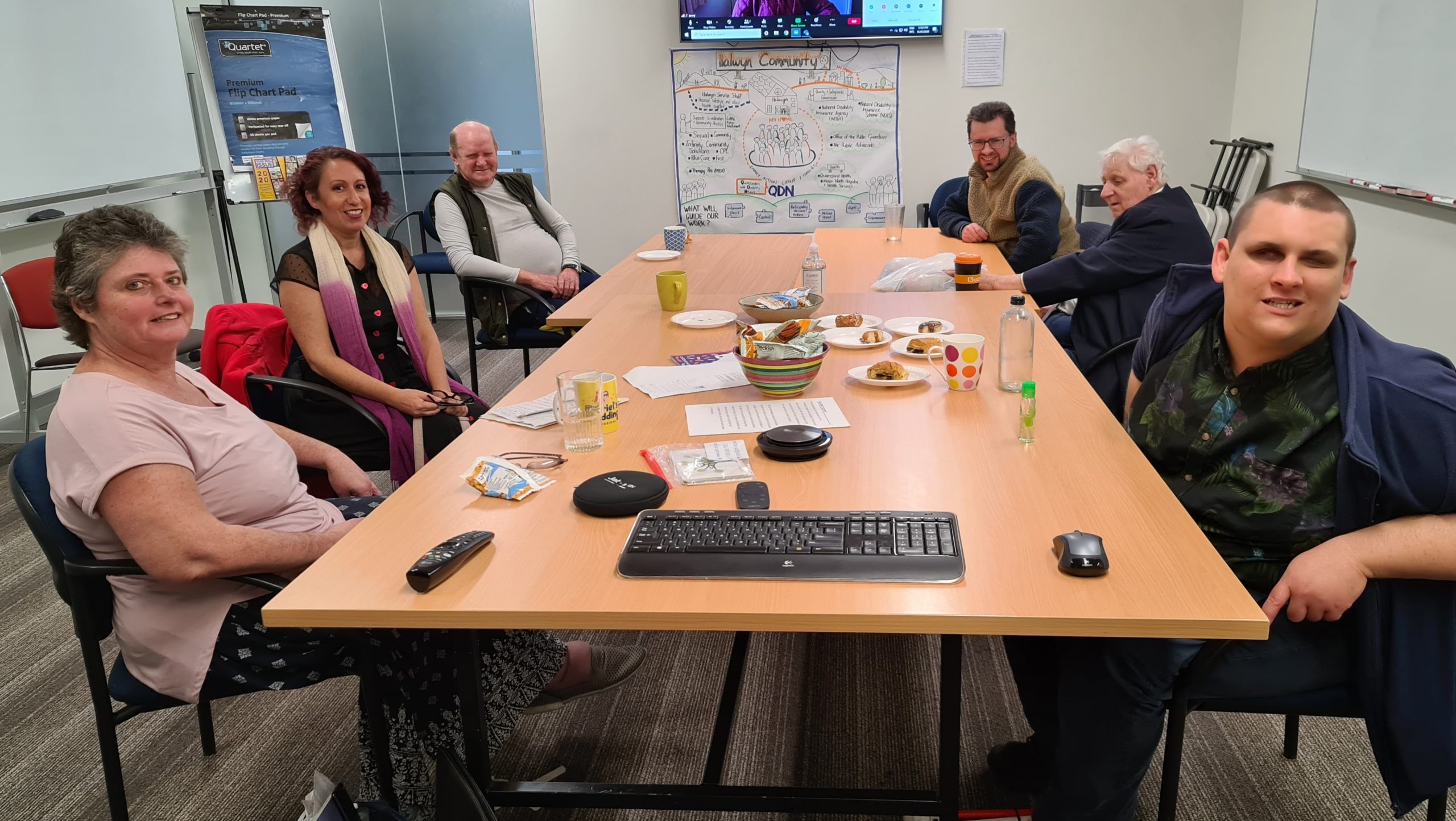 A group of men and women sitting around a conference table having a meeting, everyone is looking at the camera and smiling for the photo.
