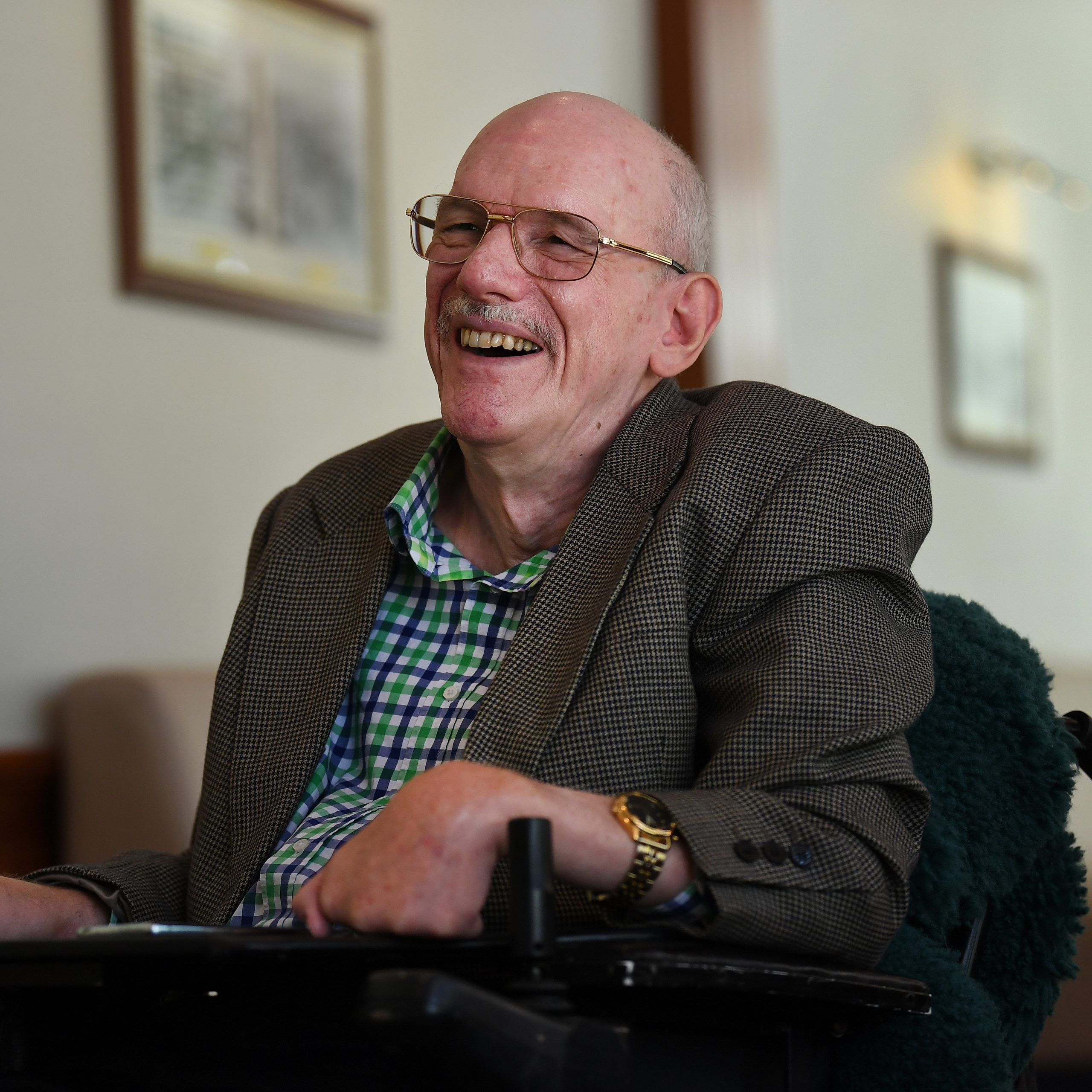 A man wearing a grey jacket and a green striped business shirt, with glasses, laughing.