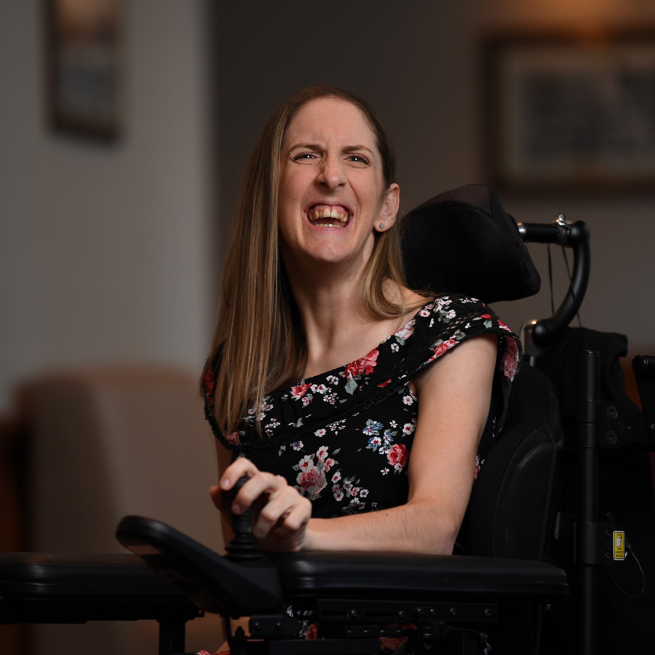 A girl with long brown hair wearing a black dress with floral print and is laughing.