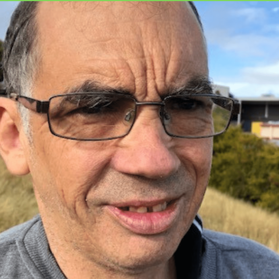 A close up photo of a mans face wearing glasses and smiling.
