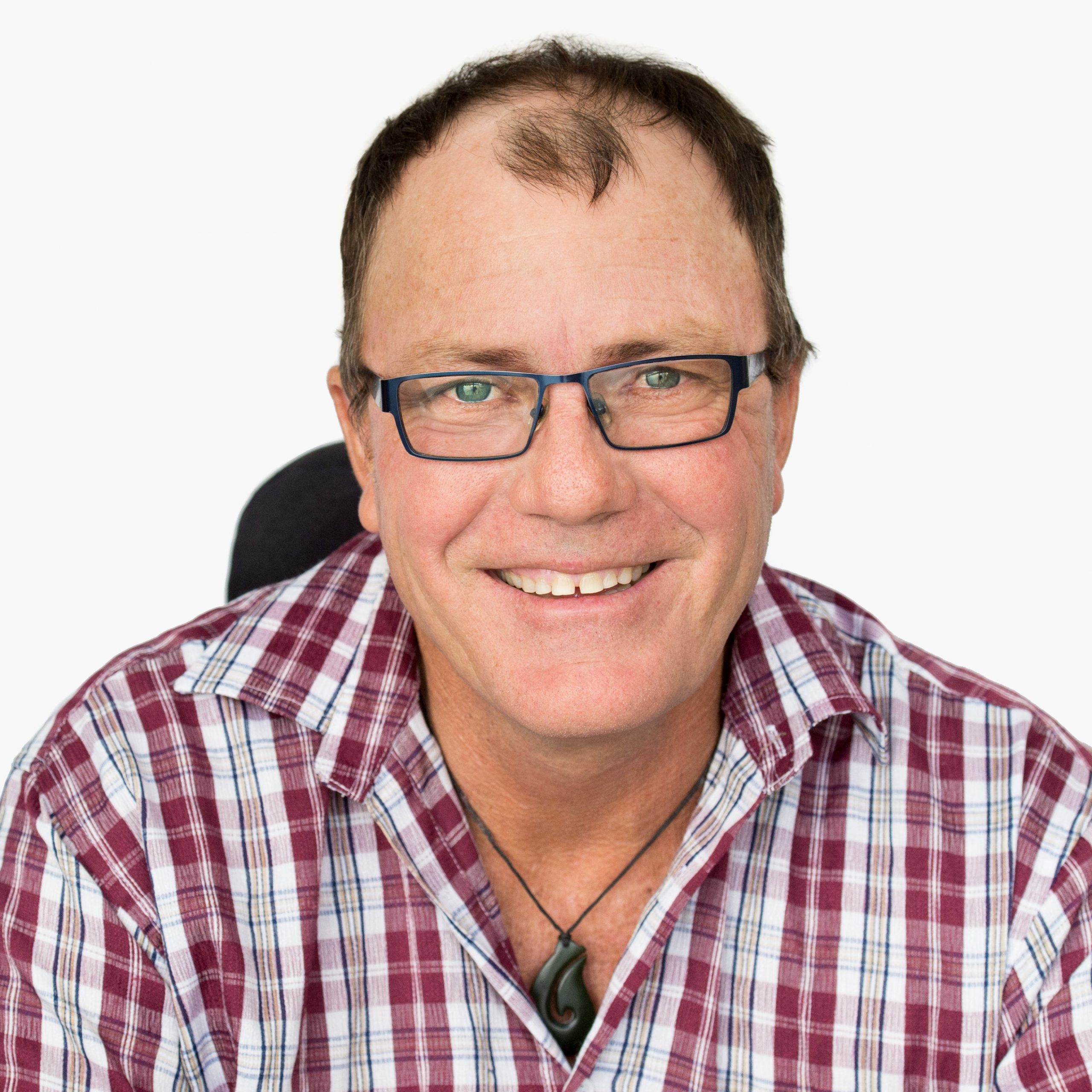 A man wearing a red and grey checked buttoned up shirt and wearing glasses and smiling at the camera.