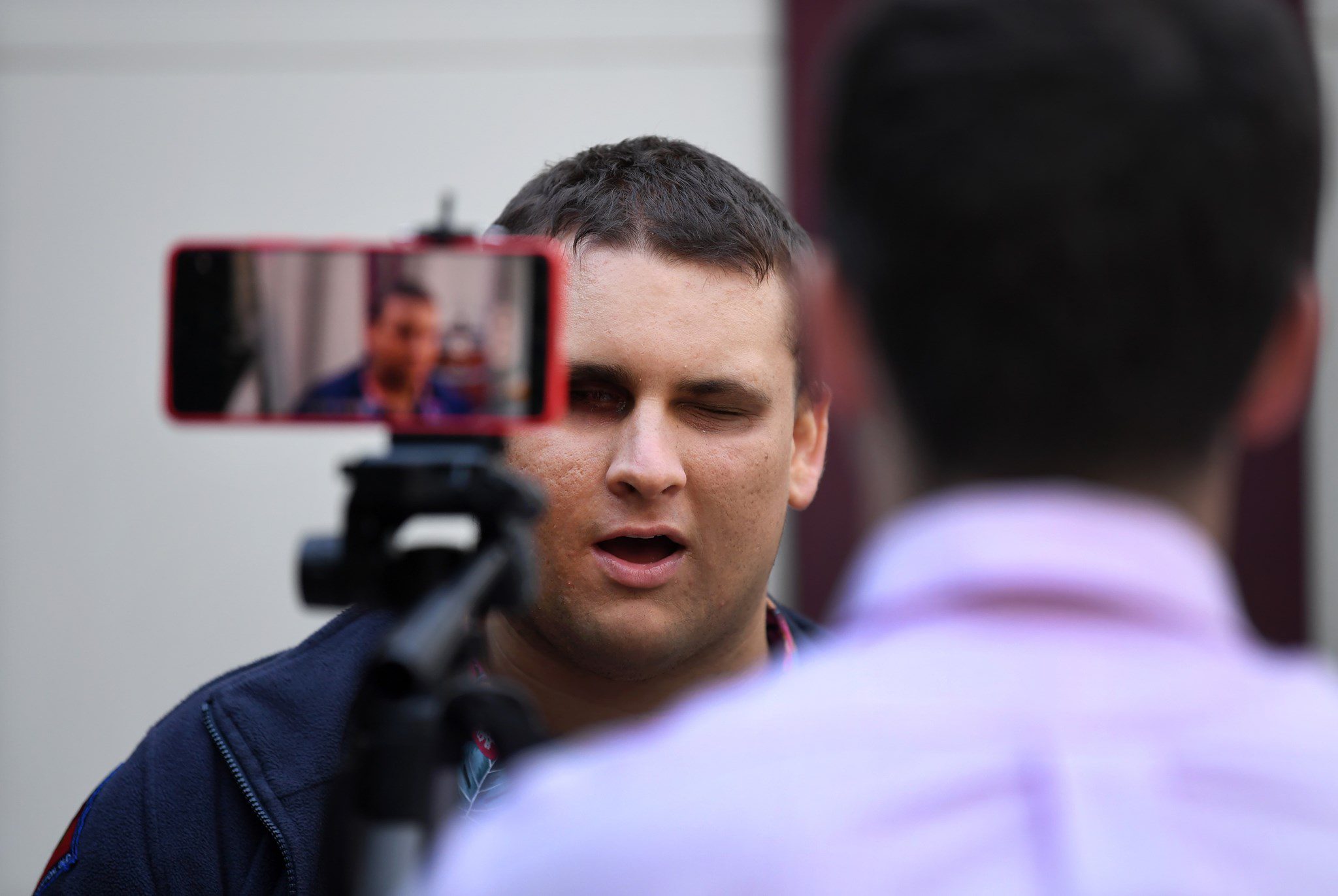 Man with his back to the camera. Another man looking at the camera being filmed on a iPhone.
