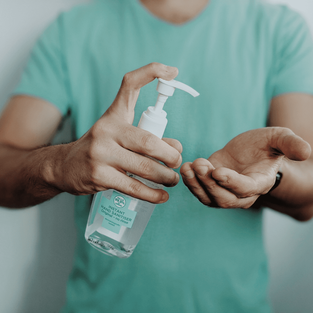 A person in a green shirt, holding a bottle of hand sanitiser and about to squirt some one their hands.