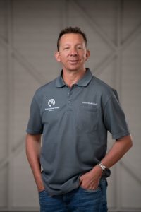 Man standing looking at camera. He has his hands in his pocket.