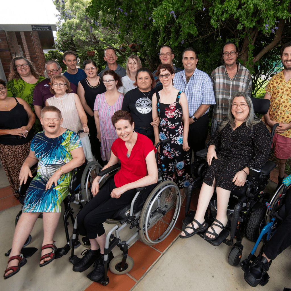 A group of people standing and some sitting in wheelchairs. All looking at the camera smiling.