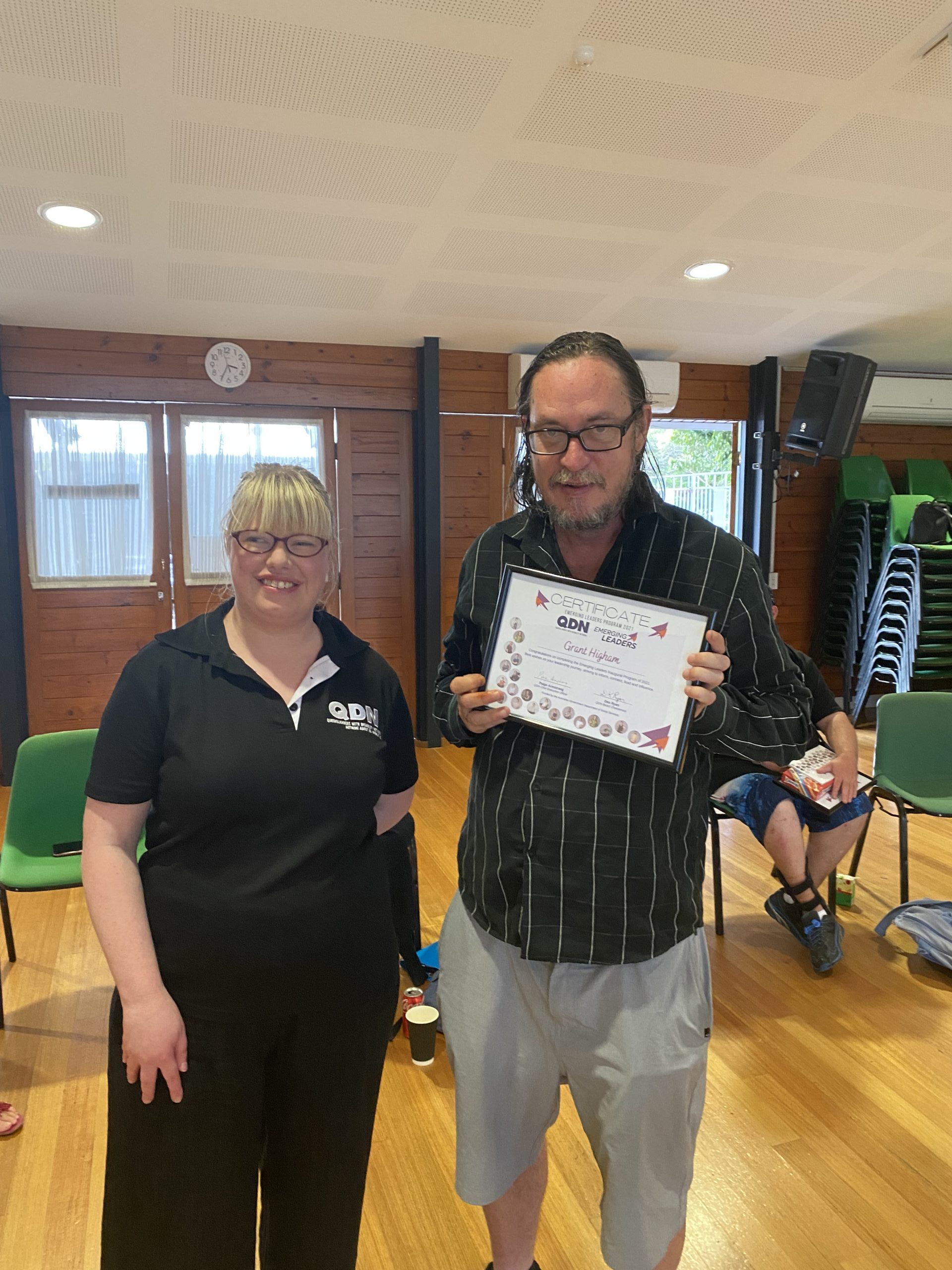 A woman and a man standing next to each other. The man is holding a certificate up and they are both looking at the camera smiling.