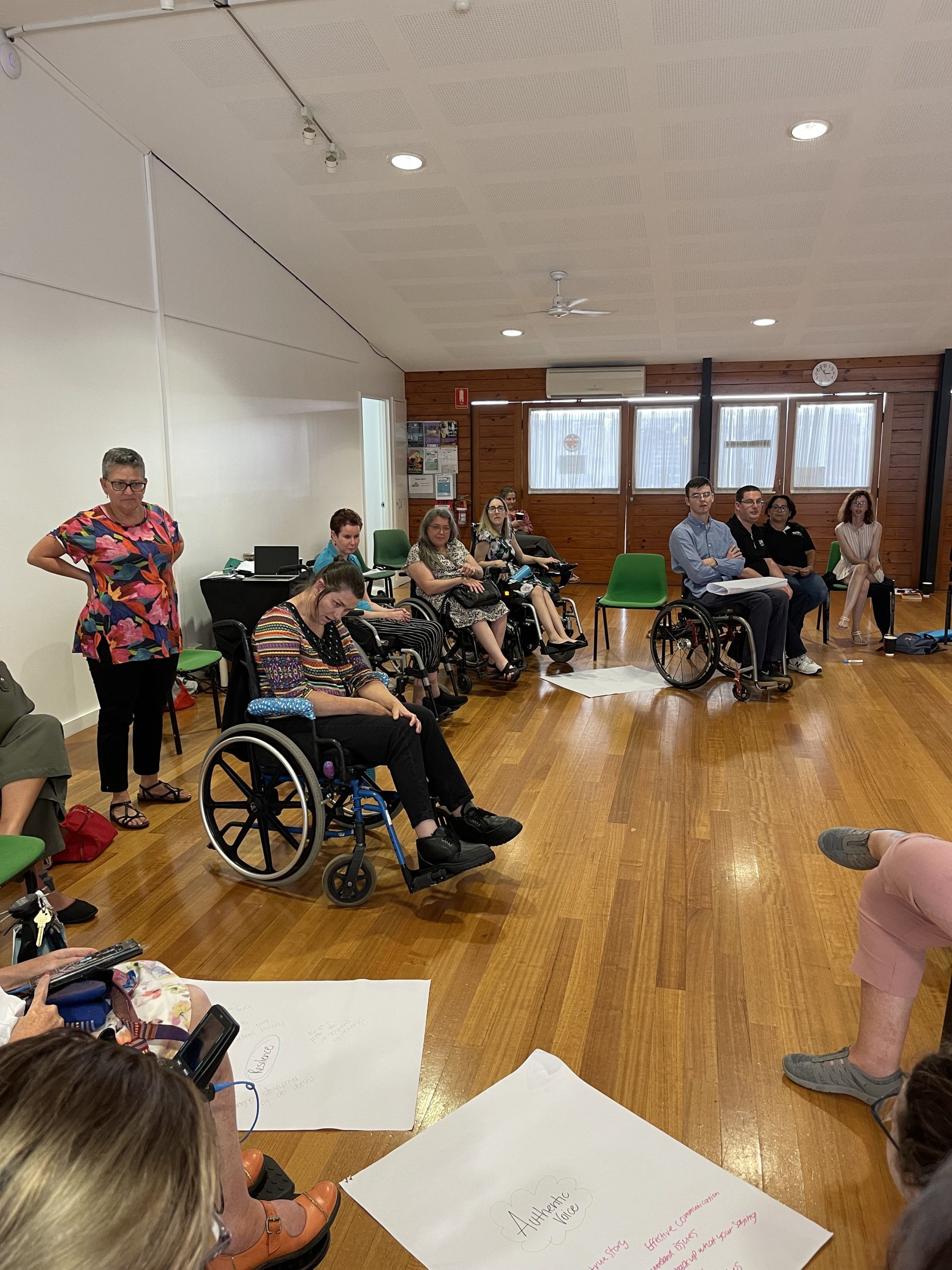 Many people sitting in a circle in a large room in a workshop setup.