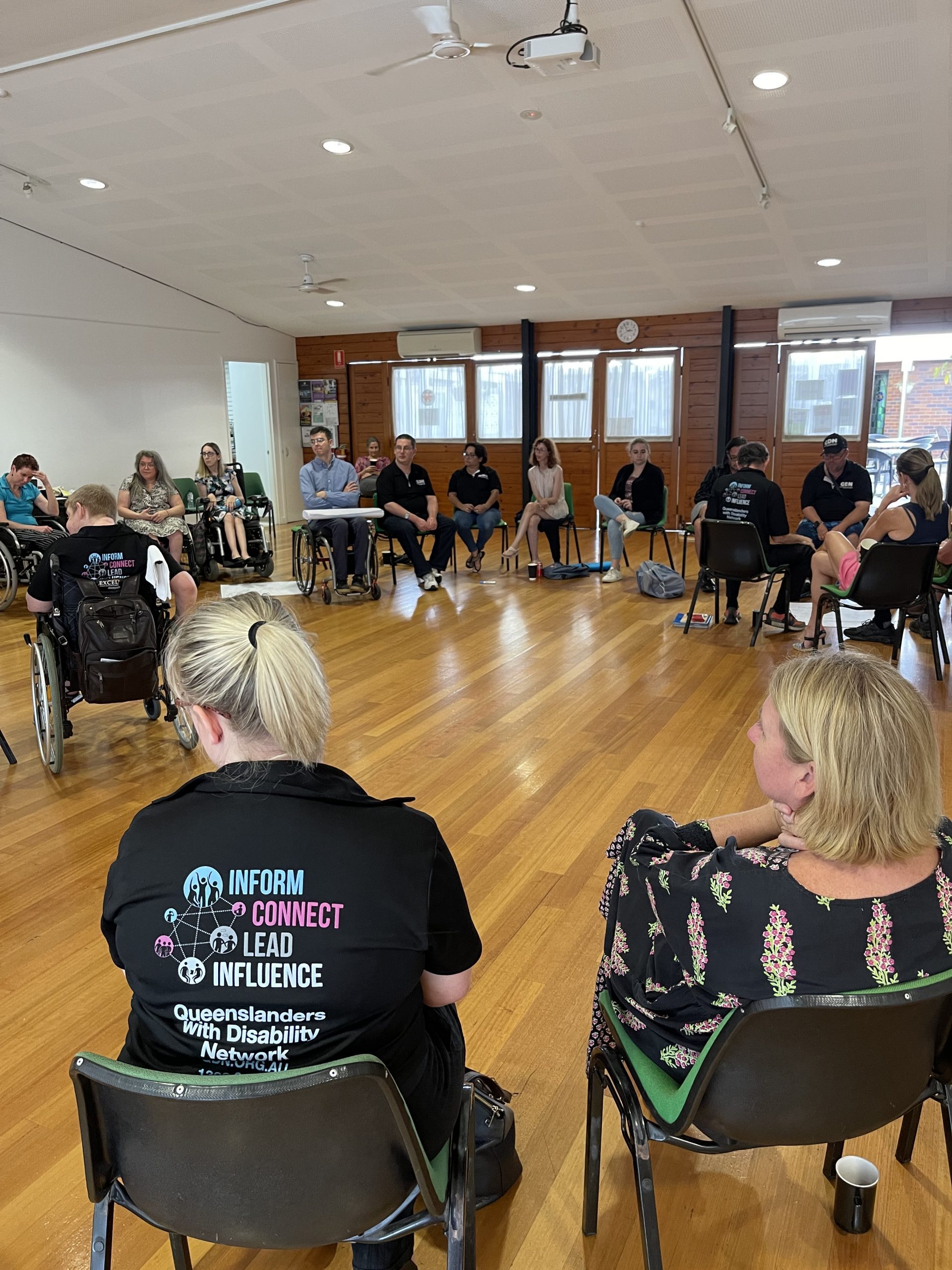Many people sitting in a circle in a large room in a workshop setup.