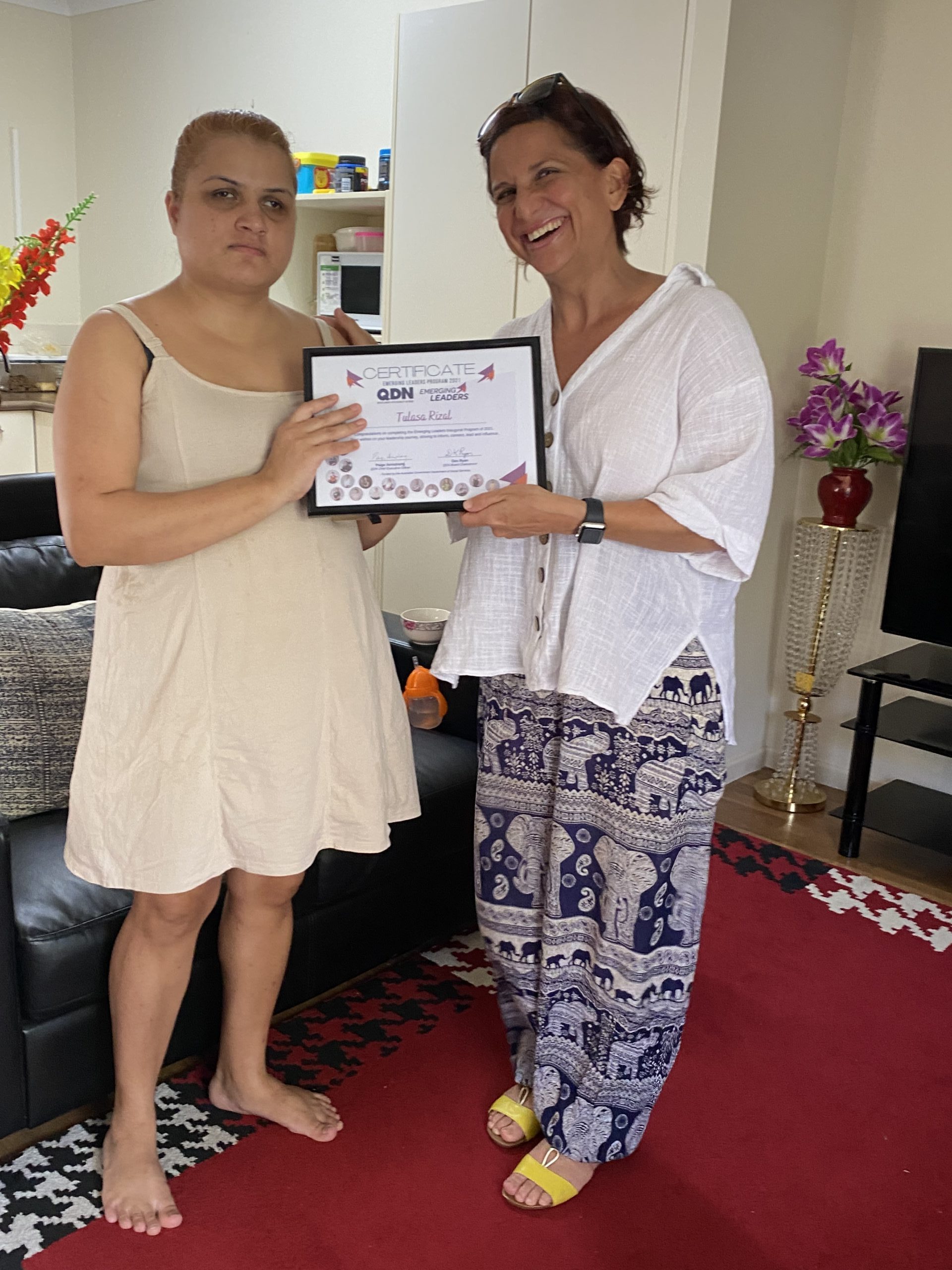 Two women standing next to each other holding a certificate in a frame and smiling at the camera.