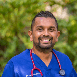 A man wearing blue hospital scrubs and a stethoscope around his neck. He has short brown hair and a beard and is smiling at the camera.