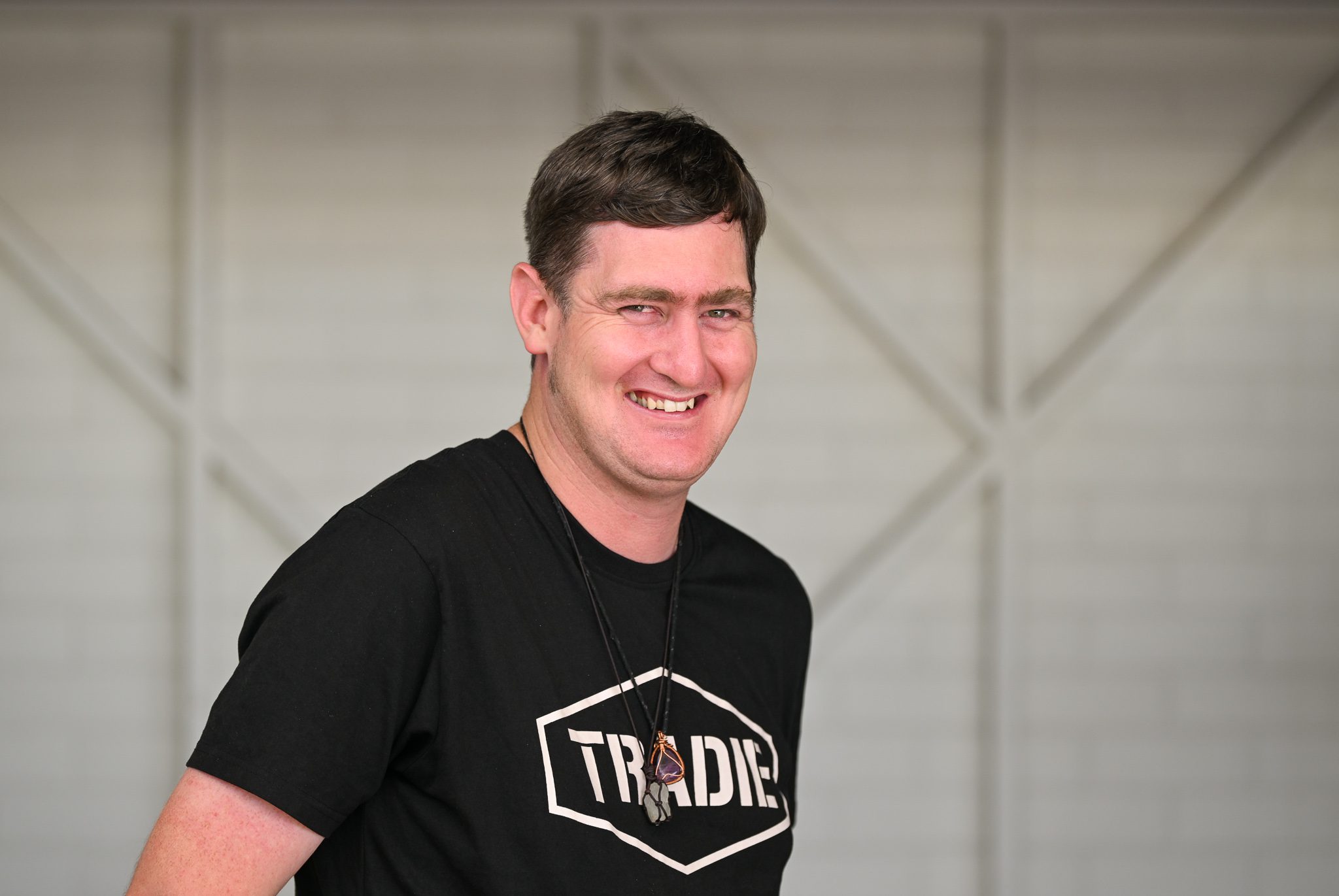 A man with short brown hair, wearing a black tshirt, smiling at the camera.