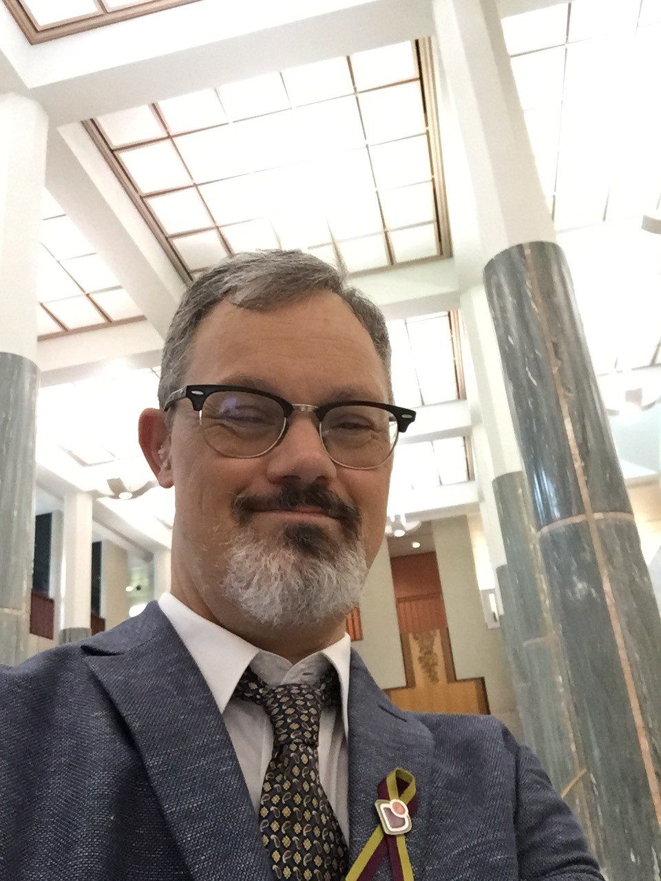 A man wearing glasses and wearing a grey suit, smiling at the camera.