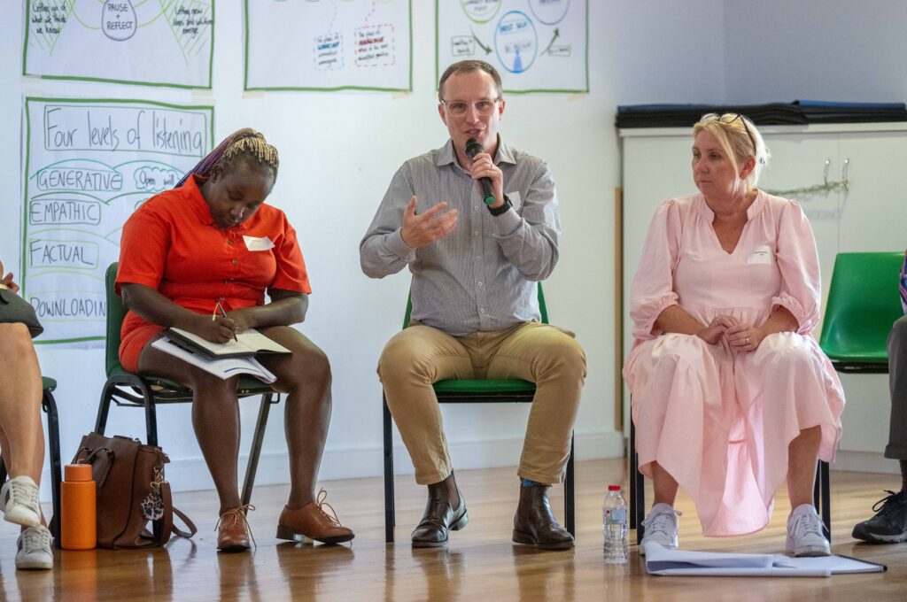 A man giving a speech at emerging leaders workshop. He is facing the camera, and there are people listening to him during the meeting.